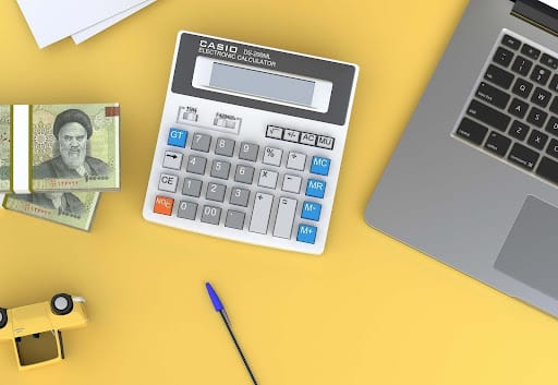 a calculator, laptop, money and pen on a table