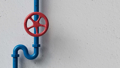 A blue pipe with a red valve handle mounted on a light gray wall.