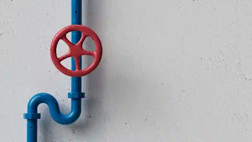 A blue pipe with a red valve handle mounted on a light gray wall.