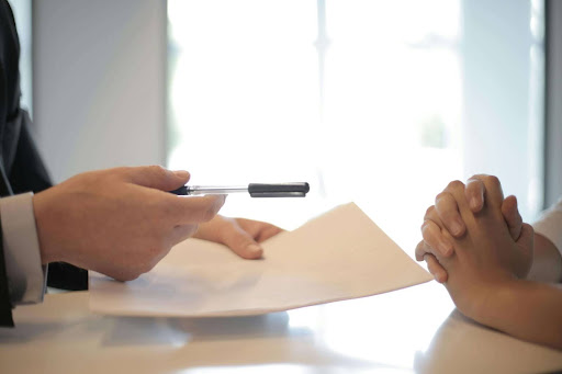 Hands of a client receiving a document and pen from an insurance representative, symbolizing a denied claim and the next steps.