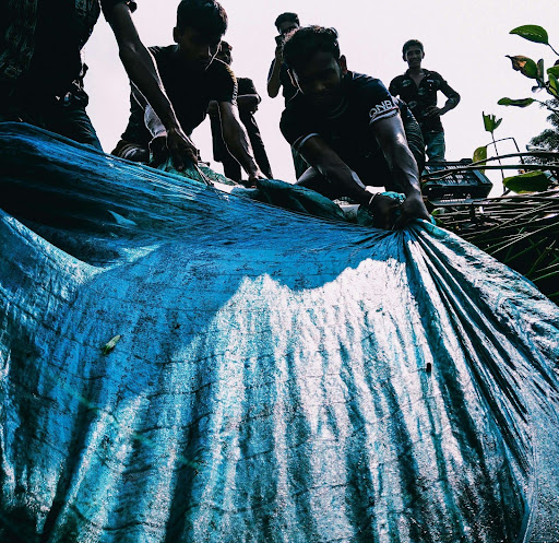 A group of individuals working together to secure a large tarp over a storm-damaged roof, highlighting the teamwork needed for effective emergency roof protection.