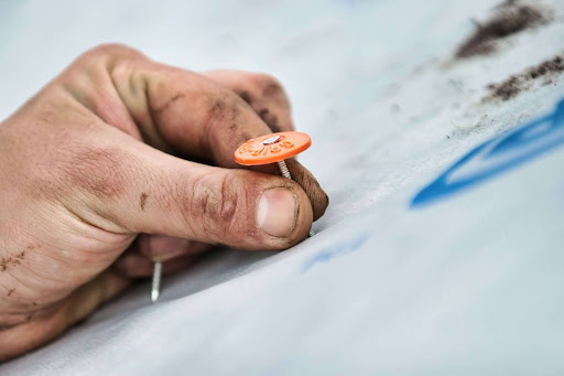 A close-up of a hand securing a tarp with a roofing nail, illustrating the step-by-step process of installing roof tarps for storm damage protection.