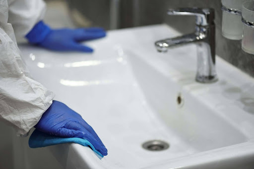 Gloved hands cleaning a bathroom sink, symbolizing maintenance to prevent water overflow.