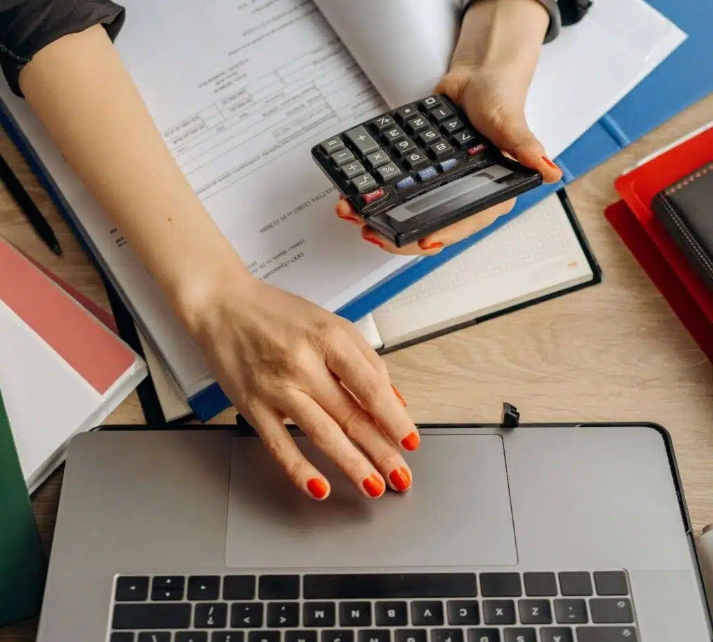 A person calculating restaurant insurance expenses using documents and a laptop.