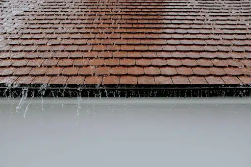 Rain streaming off of flat brown roof shingles.