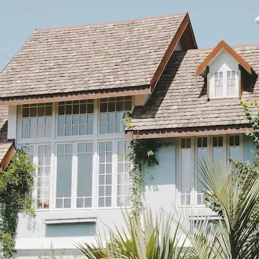 Large white house with light brown rounded roof shingles and surrounding greenery.