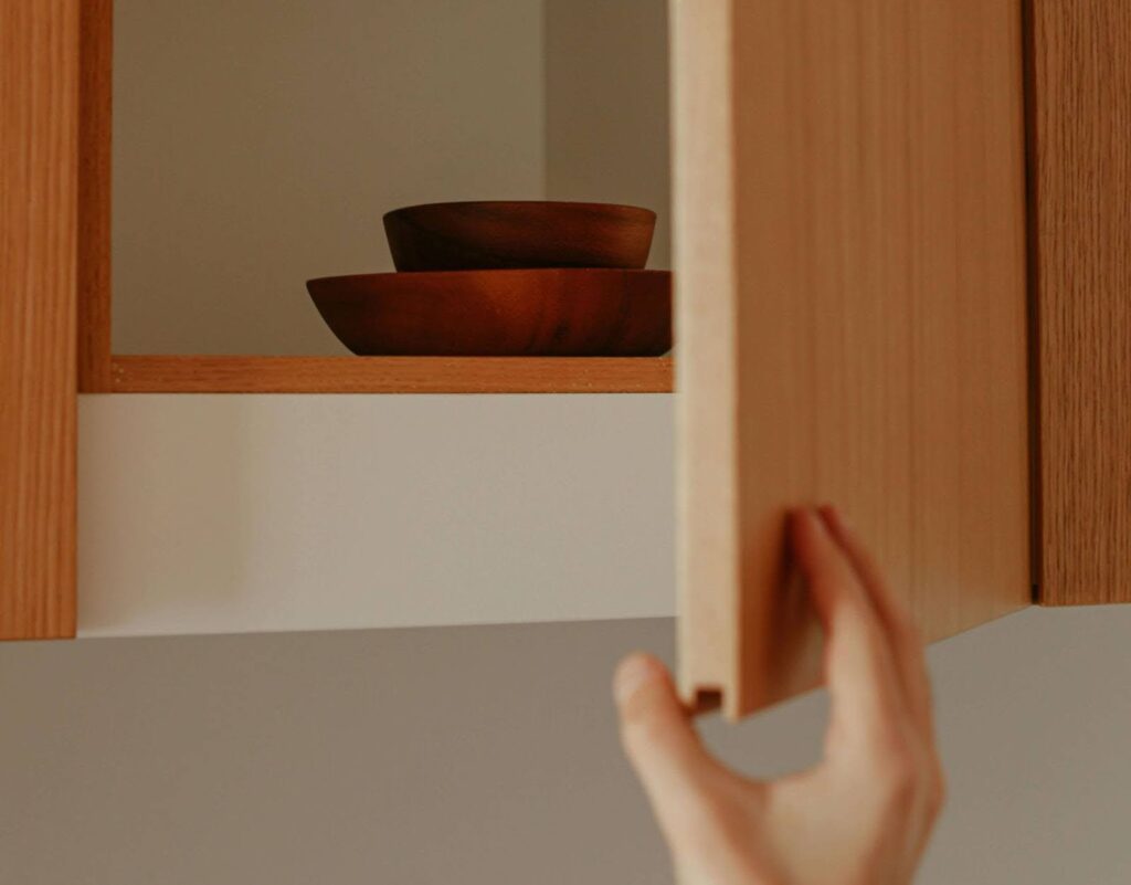 An open kitchen cabinet with two wooden bowls in it.