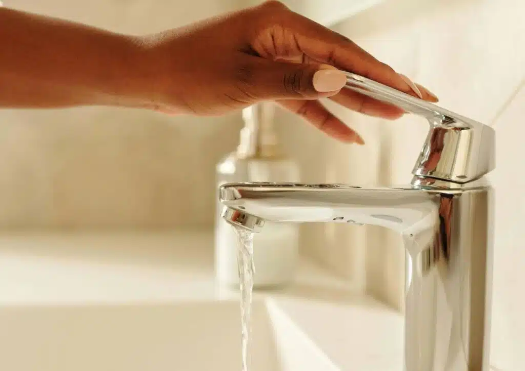 A woman gently opening a faucet.