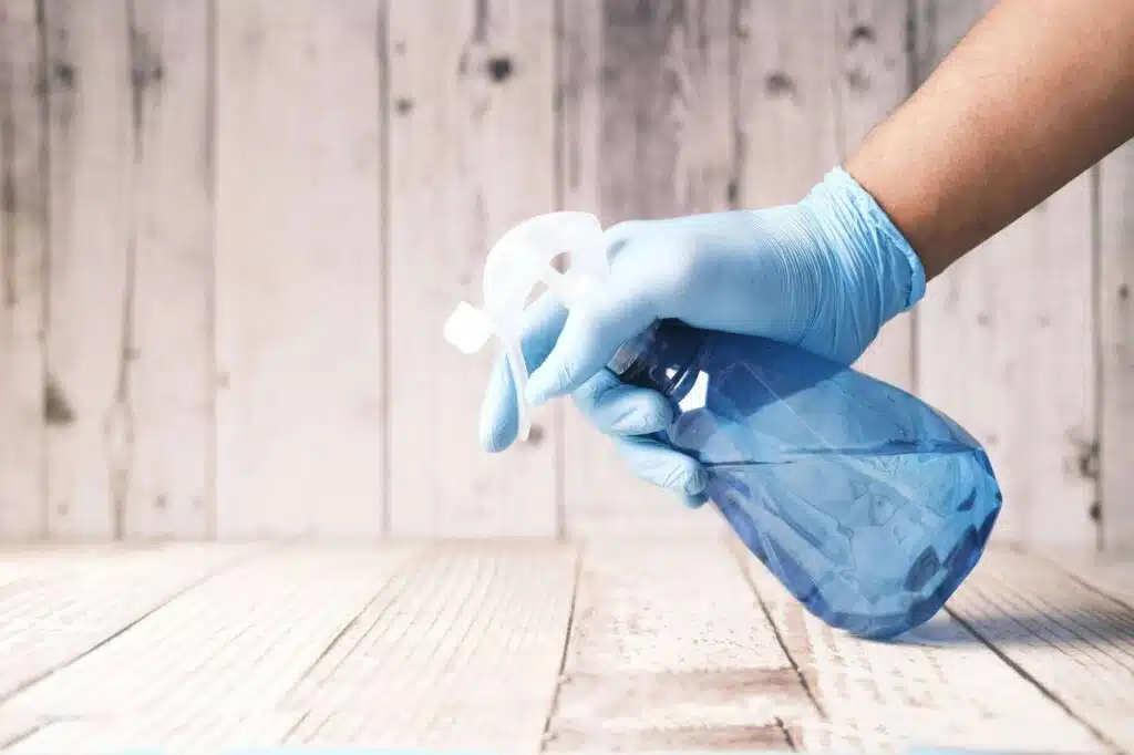 A person with blue gloves uses a spray bottle with cleaning chemicals.