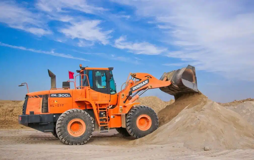 A large orange construction vehicle pouring sand on a construction site.