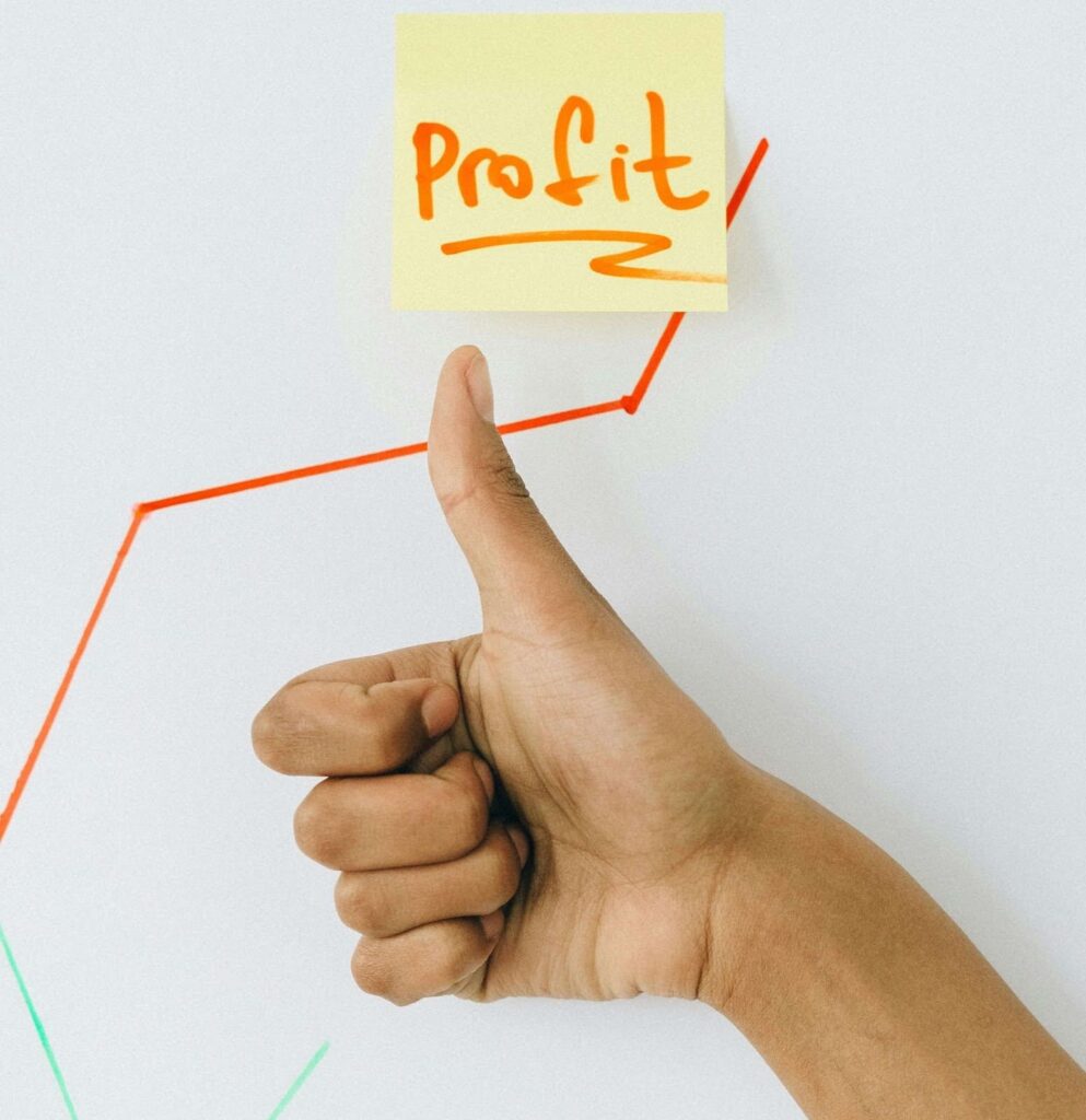 A hand giving a thumbs-up to a sticky note with the word “profit” written on it.