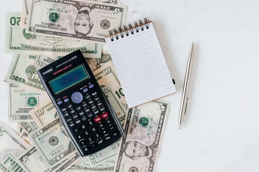 A black calculator and blank notepad on several dollar notes.