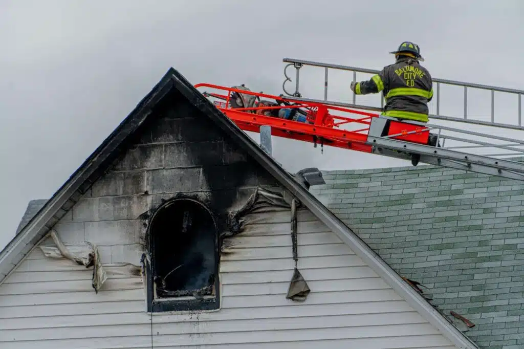 A firefighter on the roof of a home black with soot.