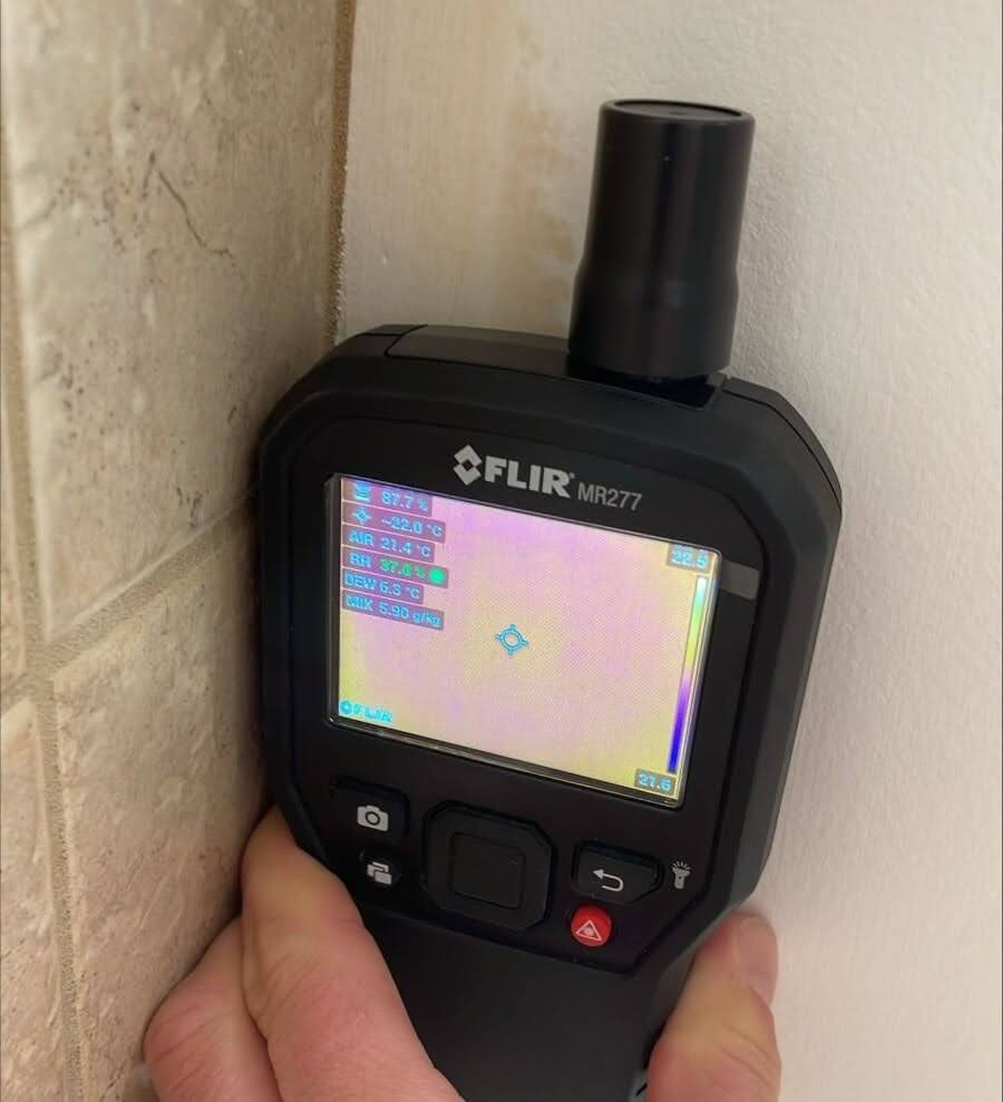 A moisture meter placed against the wall to read moisture levels.